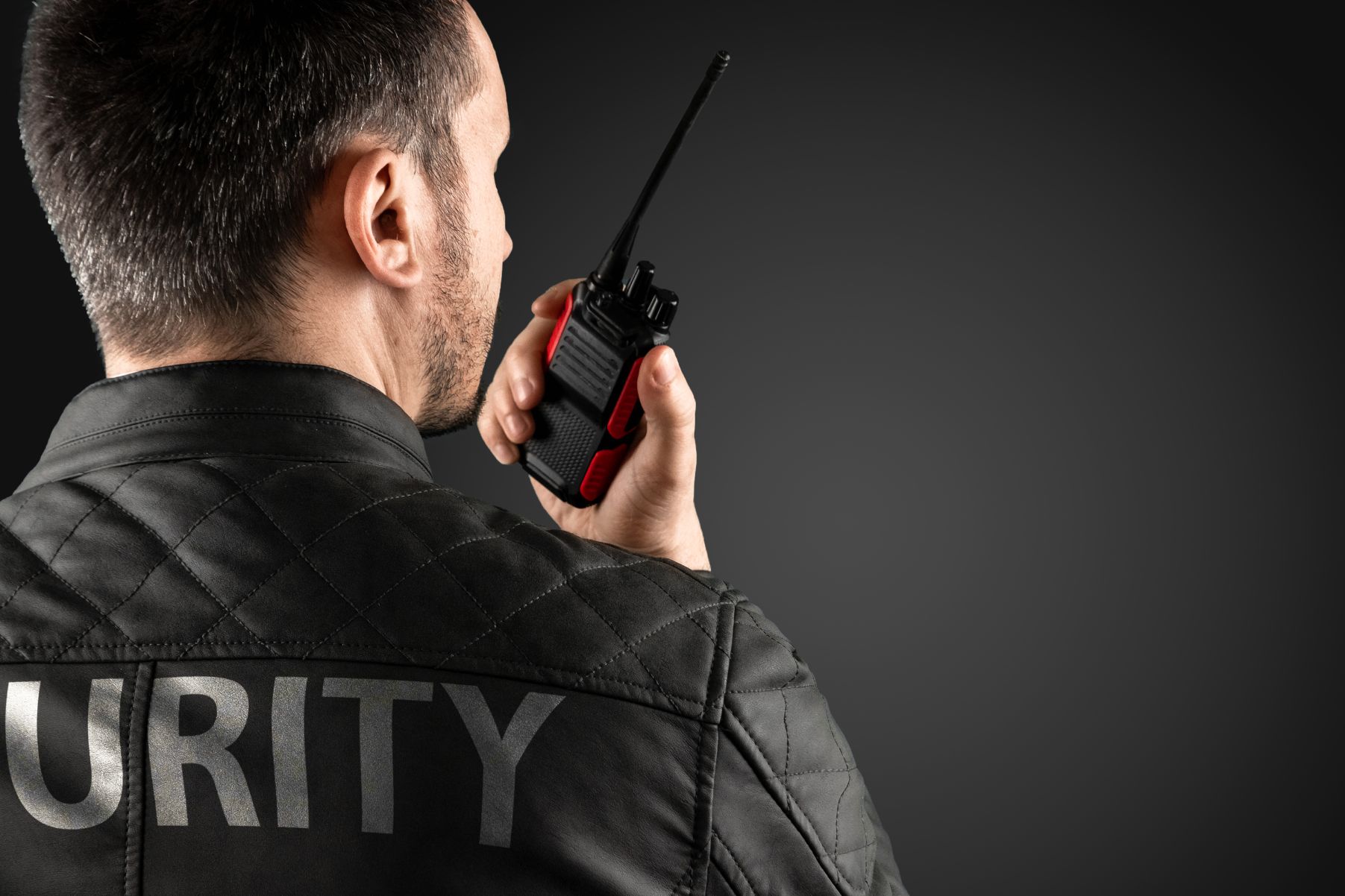 Agent de sécurité observant des écrans de vidéosurveillance et communiquant par talkie-walkie.